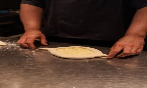 Top-down view of a traditional Georgian Adjaruli Khachapuri cheese bread topped with warm cheese, butter, and a fresh egg yolk, served on a plate.